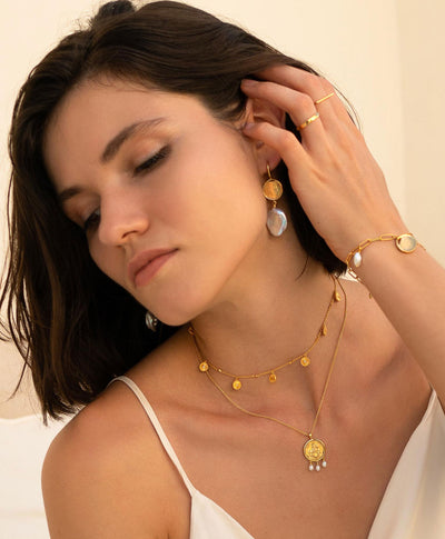Model wearing gold engraved horse coin pendant necklace with hanging freshwater pearls with coin choker with CZ crystals and freshwater pearl and coin drop earrings