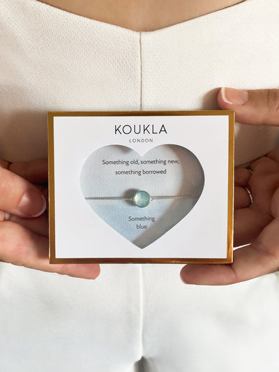 Bride holding silver bridal bracelet with blue aquamarine stone in giftable wedding packaging