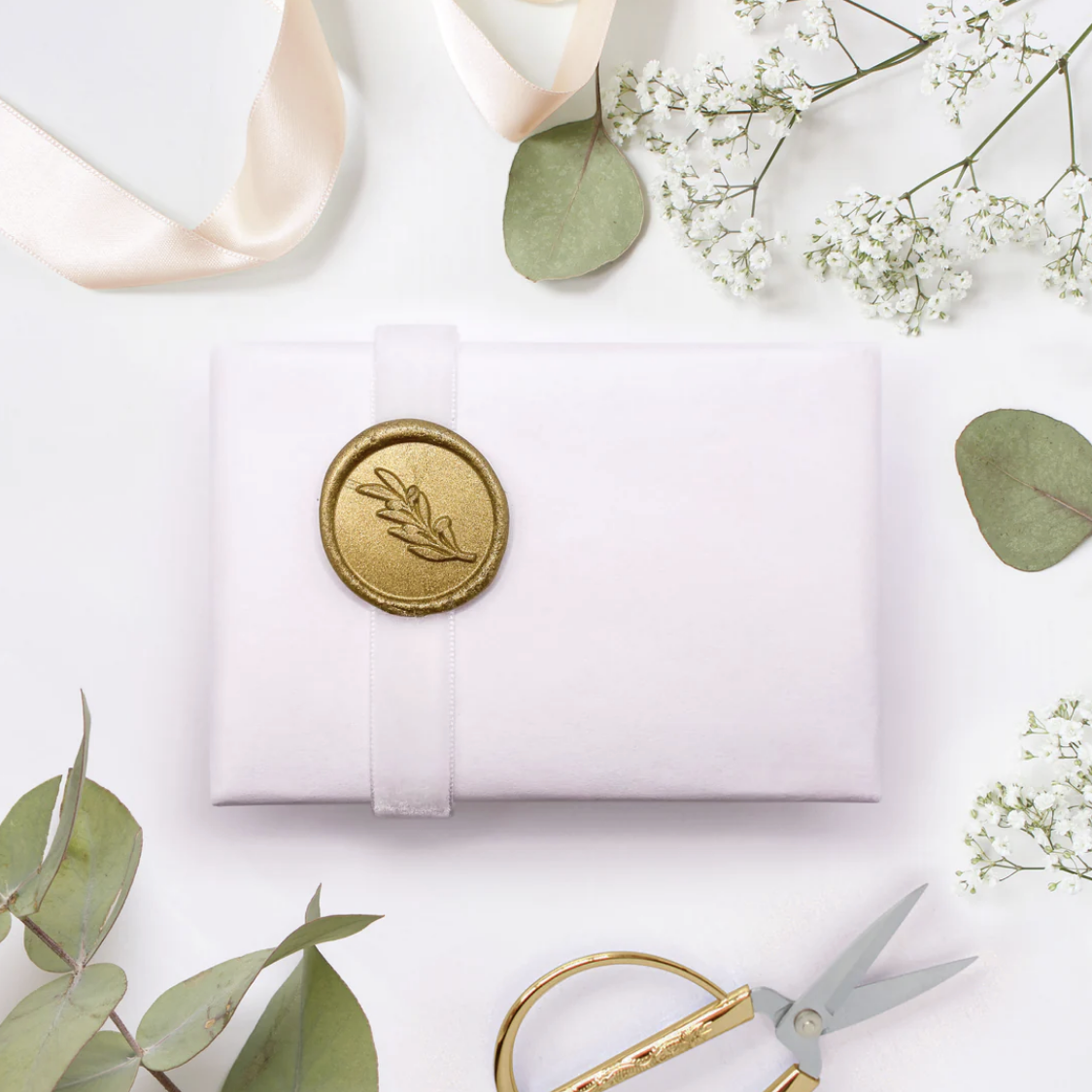 White giftwrapped jewellery box with white ribbon and gold seal