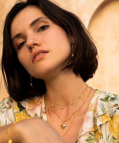 Model wearing layered gold plated sterling silver moon and star statement earrings, gold star necklace, moon pendant and matching choker with CZ crystals
