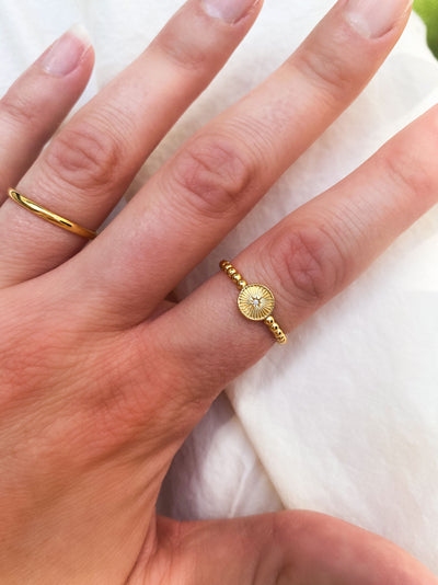 Gold ring with an engraved sun and cz crystal on a finger against a white background