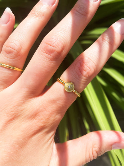 Gold ring with an engraved sun and cz crystal on a finger against a green plant