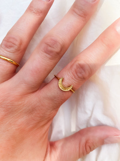 Gold ring with an engraved moon design on a finger against a white background