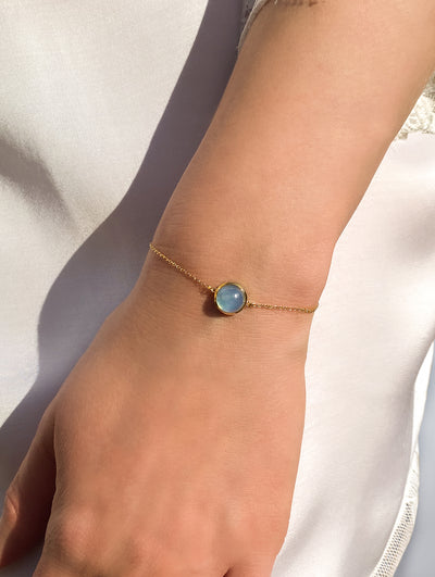 Bride wearing dainty gold bracelet with blue aquamarine stone