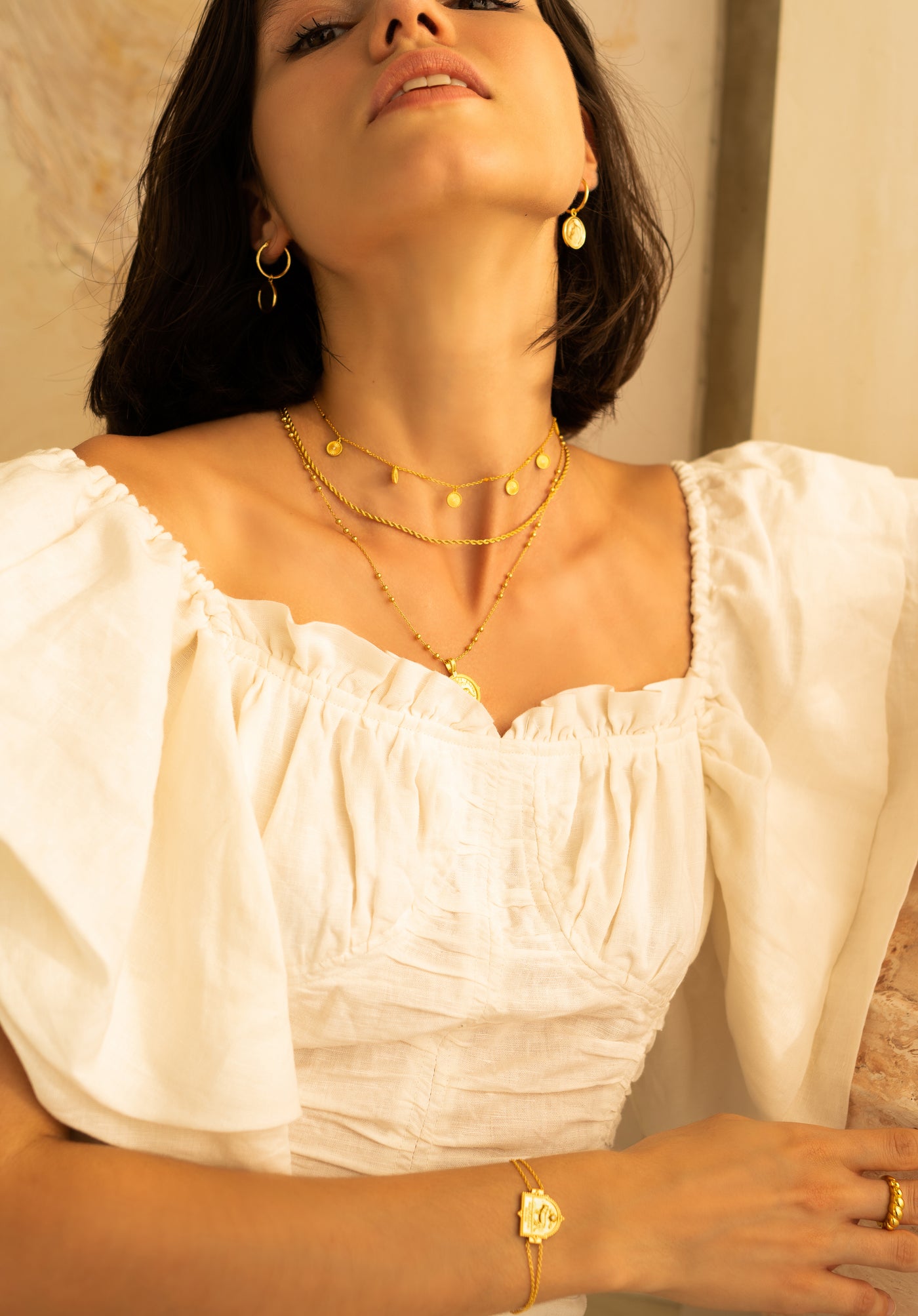 Model wearing simple gold plated sterling silver coin hoop earrings with layered necklaces, engraved bracelet and twist ring