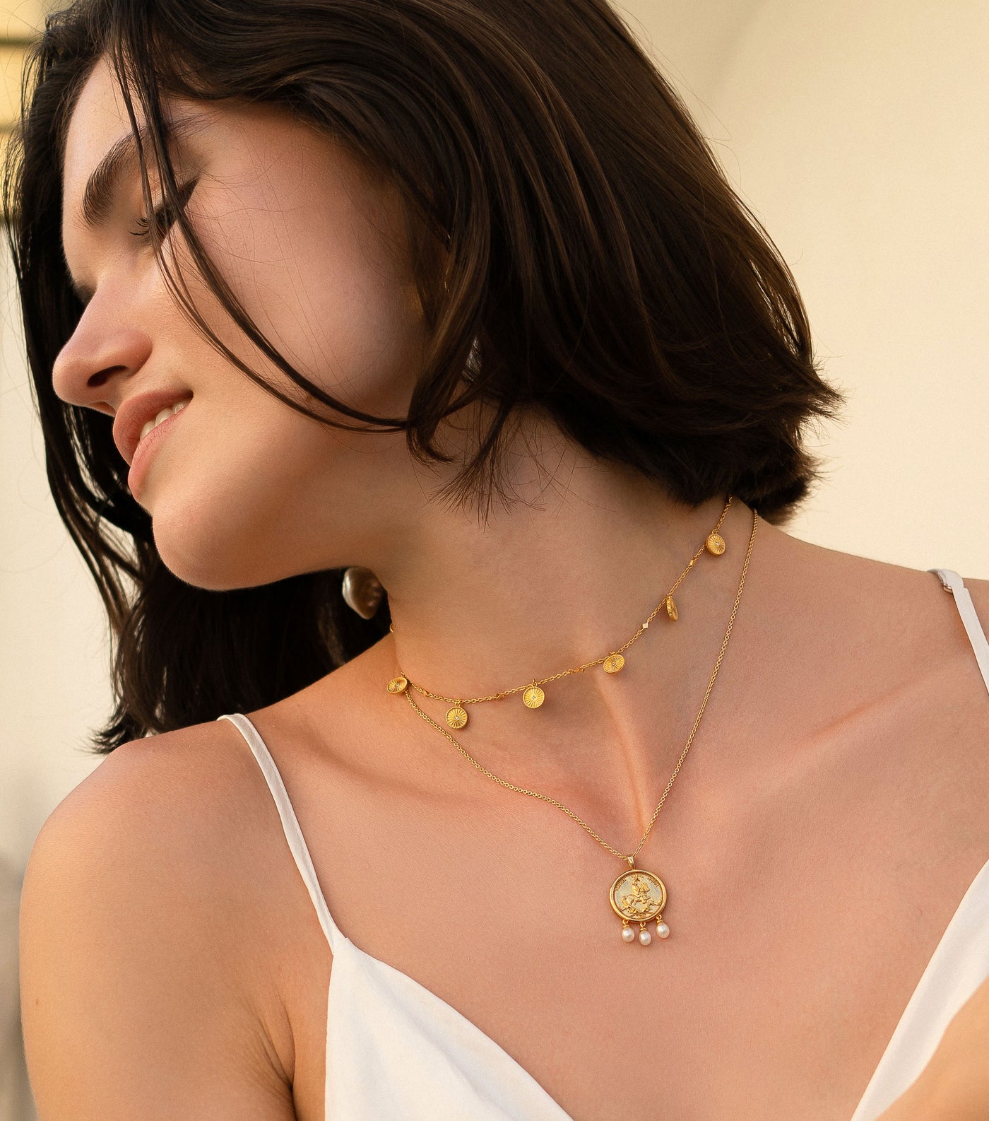 Model wearing gold engraved horse coin pendant necklace with hanging freshwater pearls and coin choker with CZ crystals