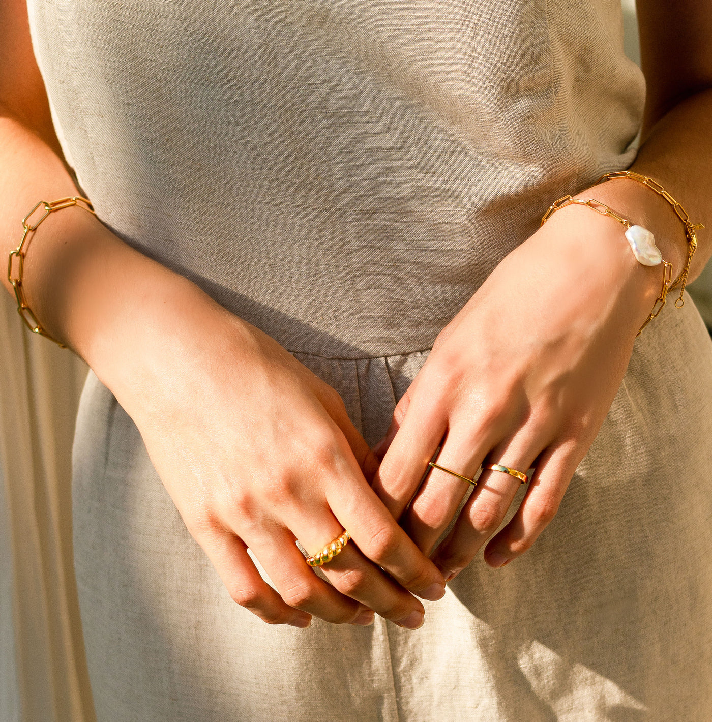 Model wearing simple gold plated sterling silver plain, minimal ring bands with chunky rope ring and pearl chain bracelets