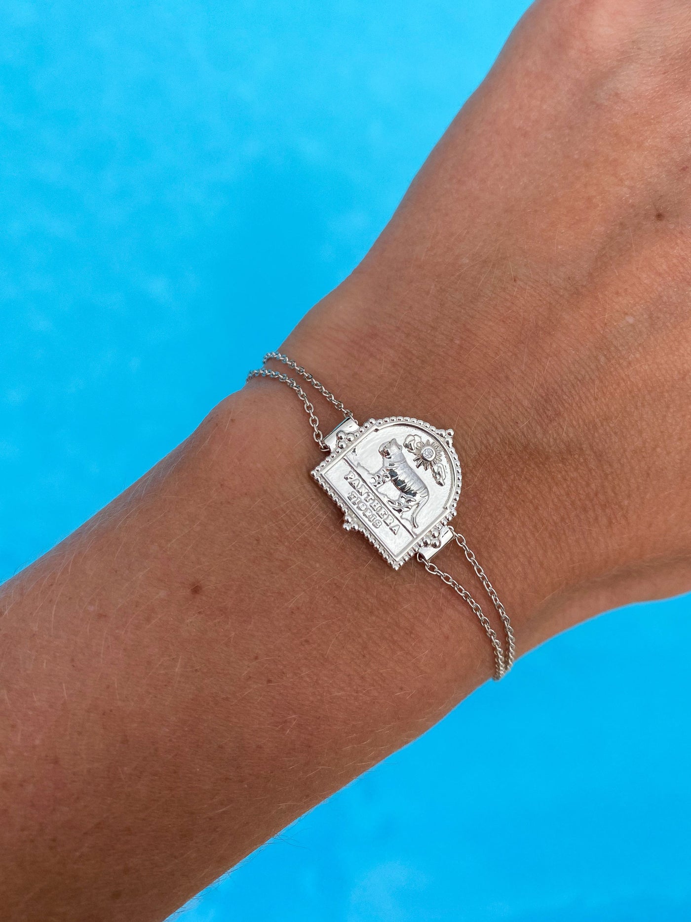 Model wearing sterling silver double chain bracelet featuring engraved tiger charm, against a blue background