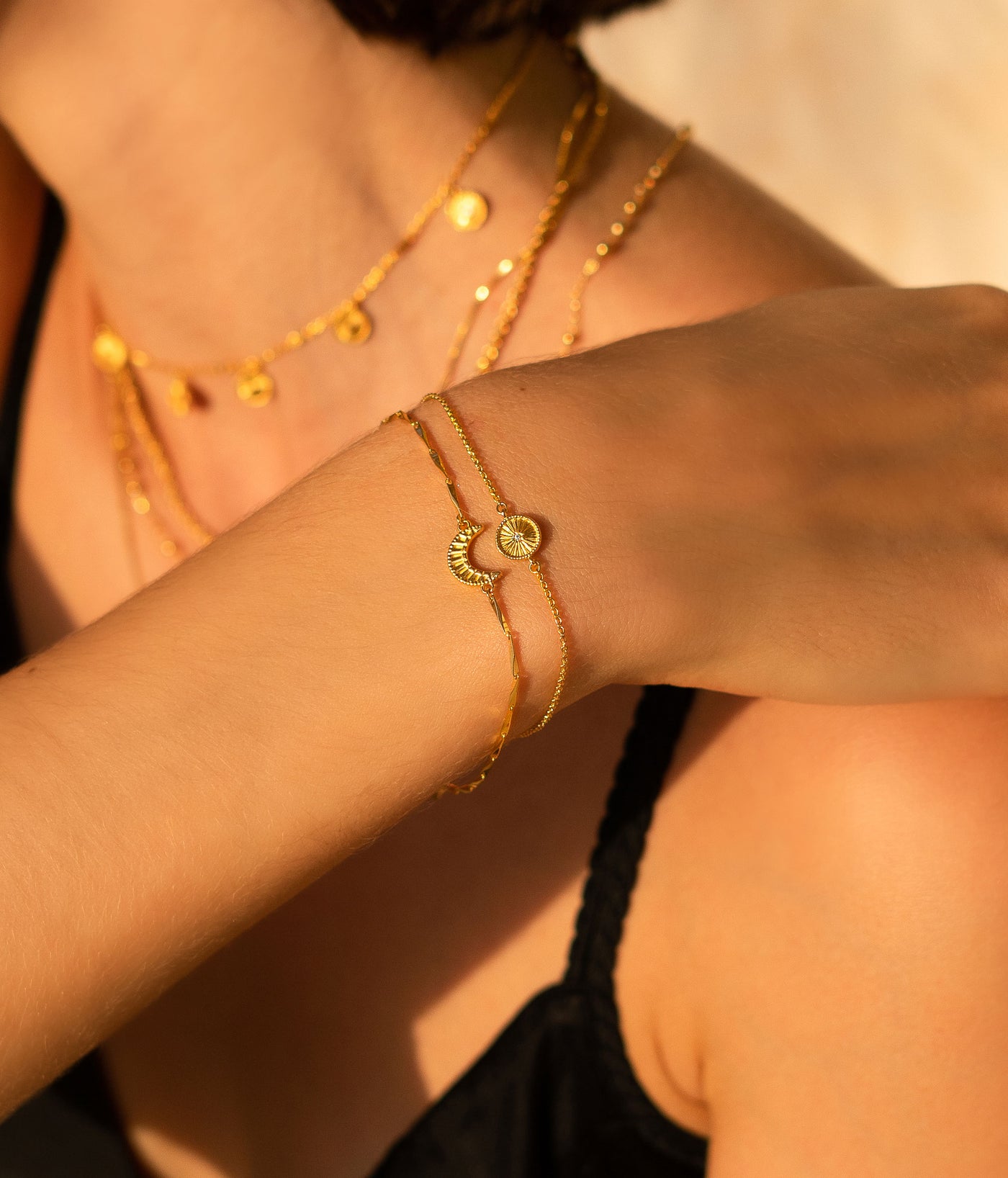 Model wearing gold plated sterling silver engraved set of 2 delicate sun and moon bracelets with CZ crystals