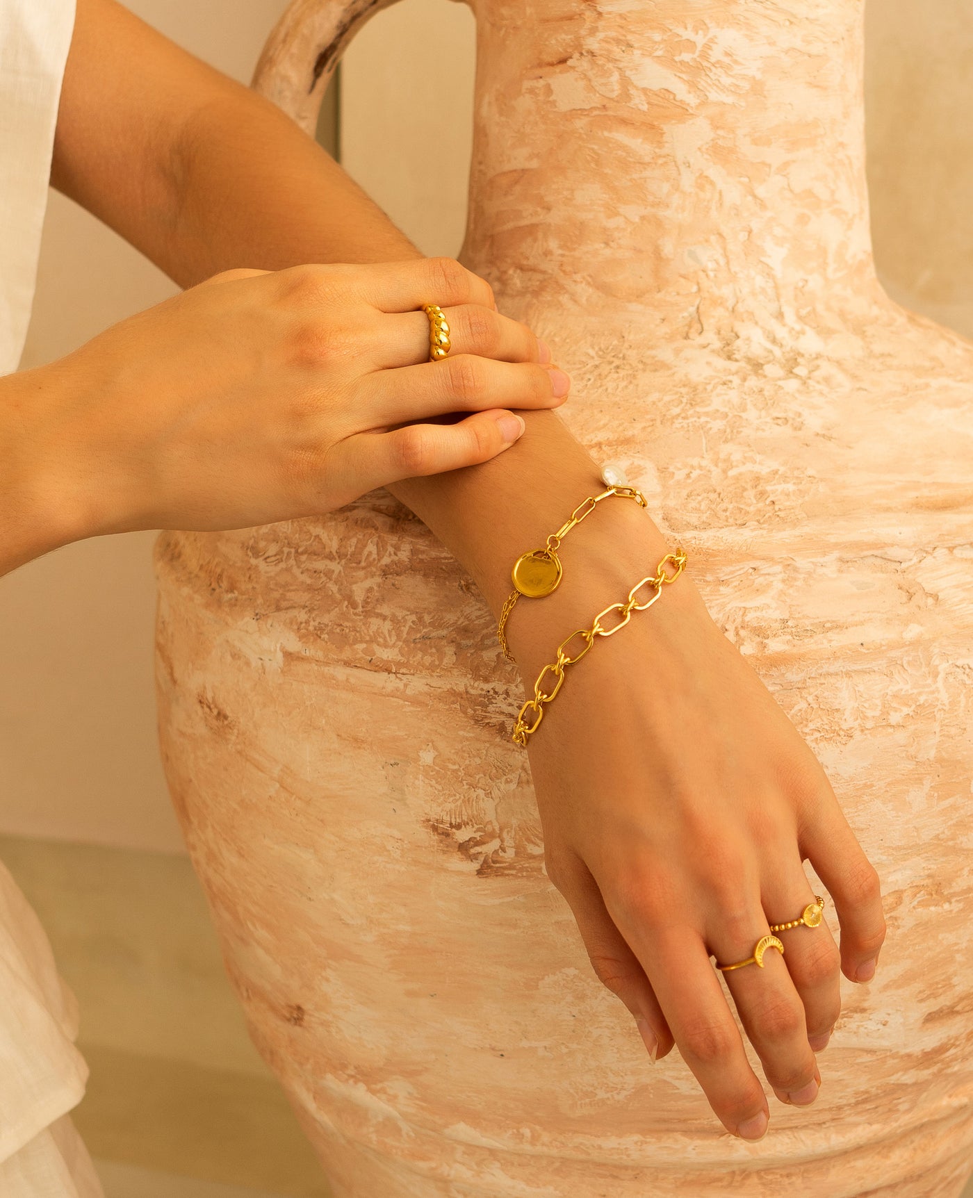 Model wearing gold plated sterling silver criss-cross link chunky chain bracelet with coin and pearl bracelet and engraved rings