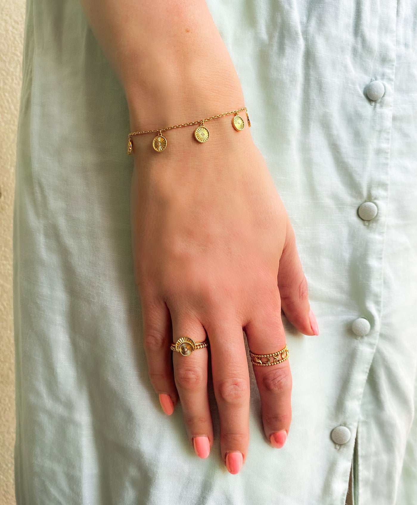 Model wearing gold plated sterling Silver bracelet with engraved coin hanging charms featuring CZ crystals with selection of rings