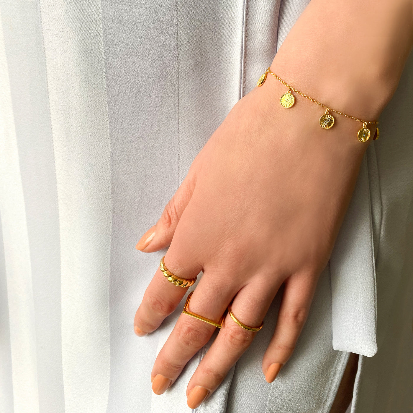 Model wearing gold plated sterling Silver bracelet with engraved coin hanging charms featuring CZ crystals with selection of rings