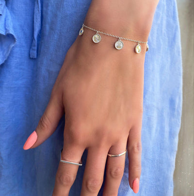 Model wearing gold plated sterling Silver bracelet with engraved coin hanging charms featuring CZ crystals with selection of rings