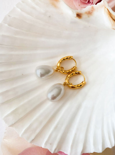 Gold plated sterling silver textured hoop drop earrings featuring freshwater pearls lying on shell