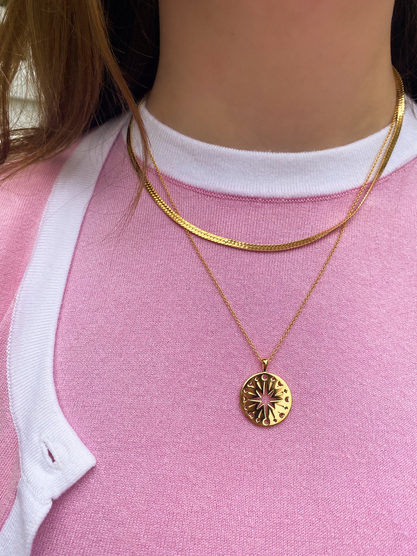 Model in pink and white outfit wearing gold filigree moon and star coin pendant with gold snake chain