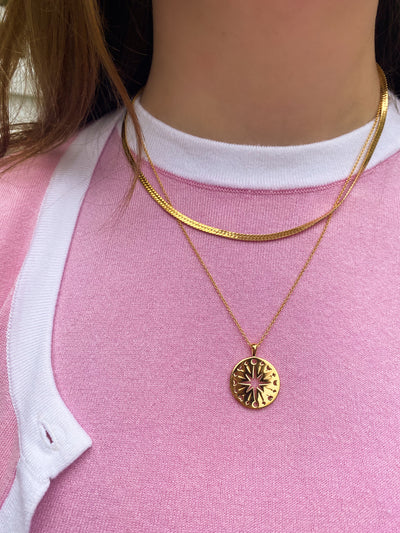 Model in pink and white outfit wearing gold filigree moon and star coin pendant with gold snake chain