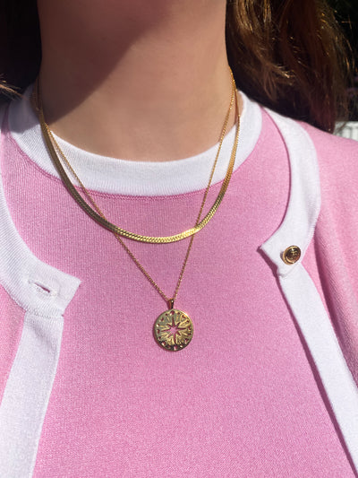 Model in pink and white outfit wearing gold filigree moon and star coin pendant with gold snake chain