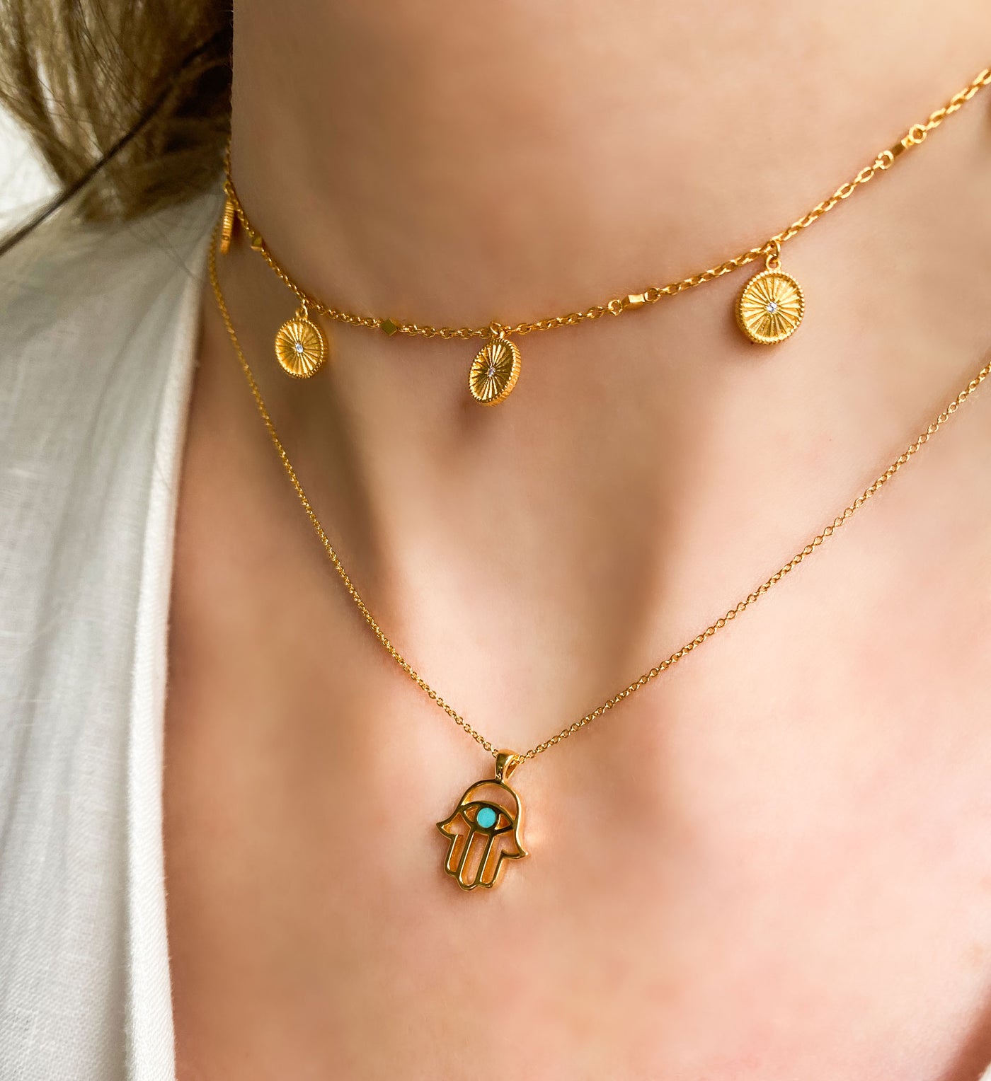 Model wearing gold plated sterling silver hamsa hand necklace with aquamarine semi-precious stone and coin choker 