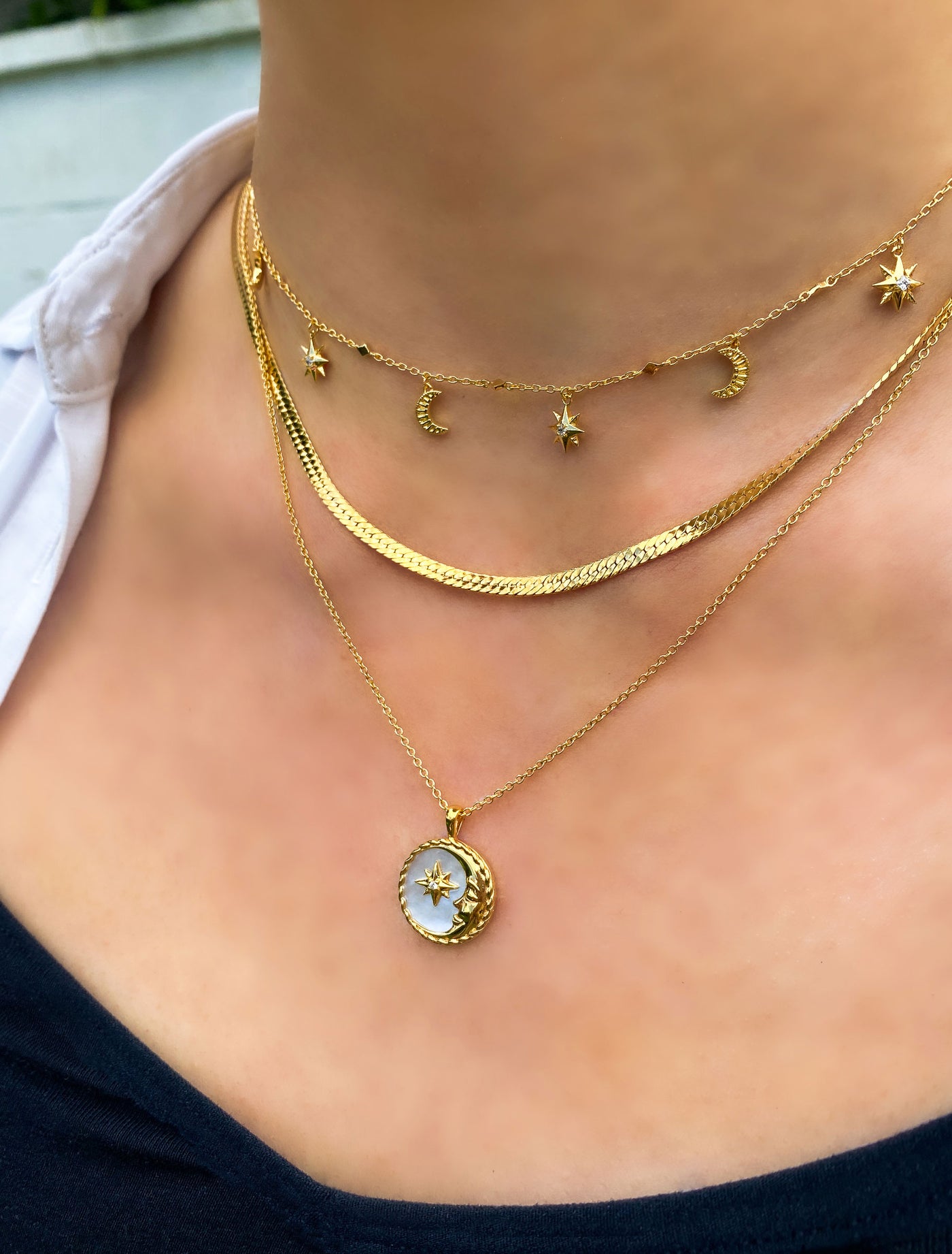 Model wearing gold moon and star choker with CZ crystals layered with snake chain necklace and engraved mother of pearl moon pendant