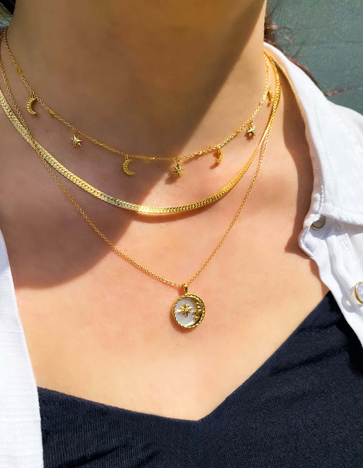 Model wearing gold moon and star choker with CZ crystals layered with snake chain necklace and engraved mother of pearl moon pendant