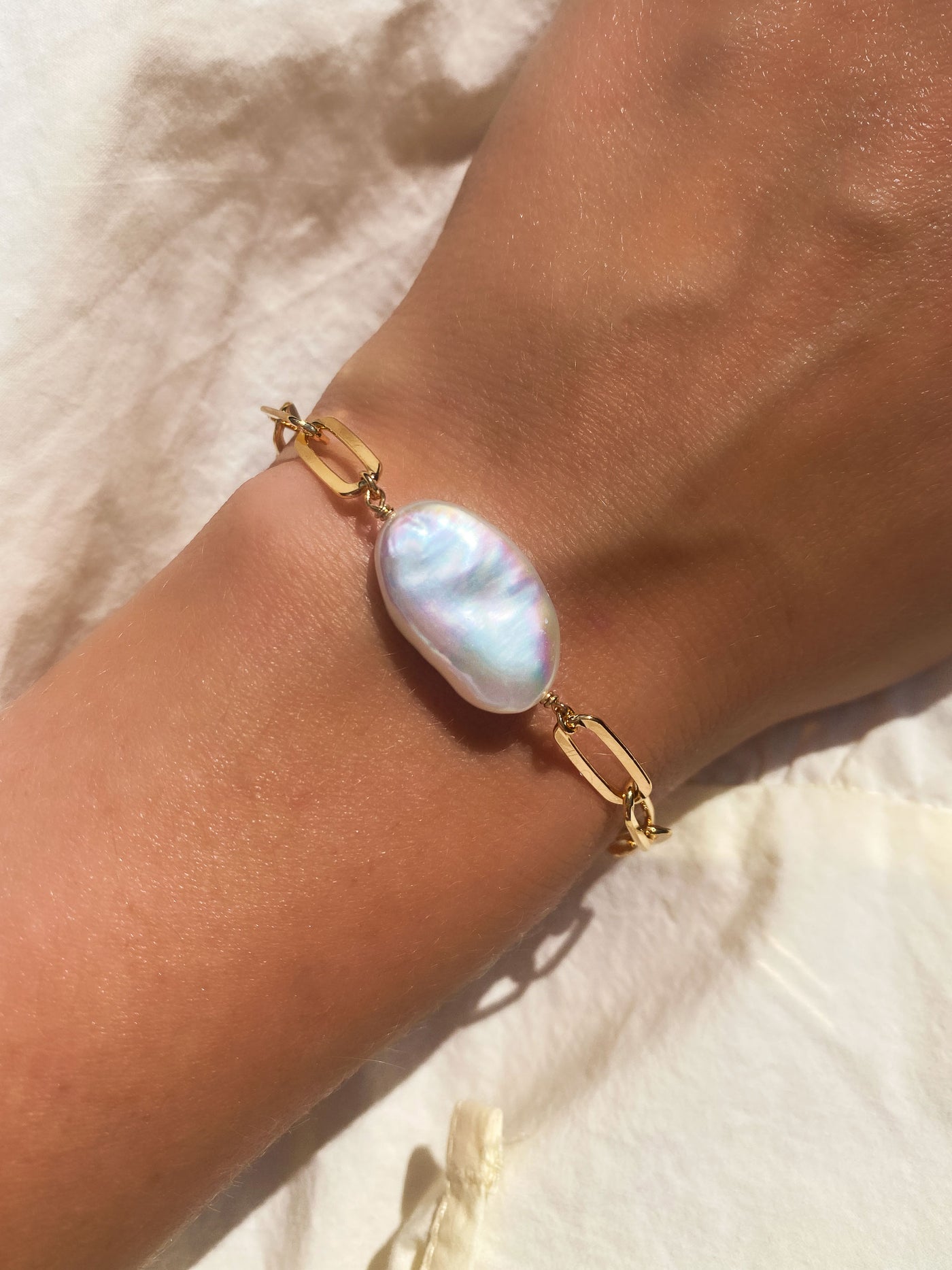 Gold chain bracelet with a large freshwater pearl on a wrist against a light background