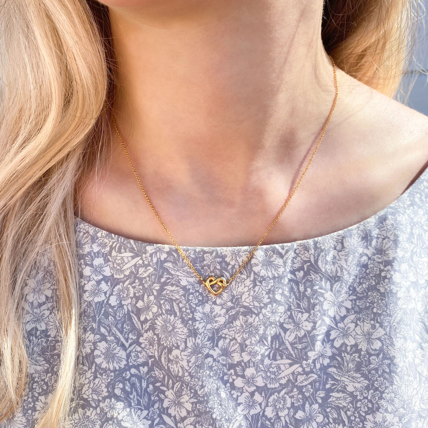 Model wearing 18kt Gold plated sterling silver heart knot necklace for bridesmaid in giftable heart packaging