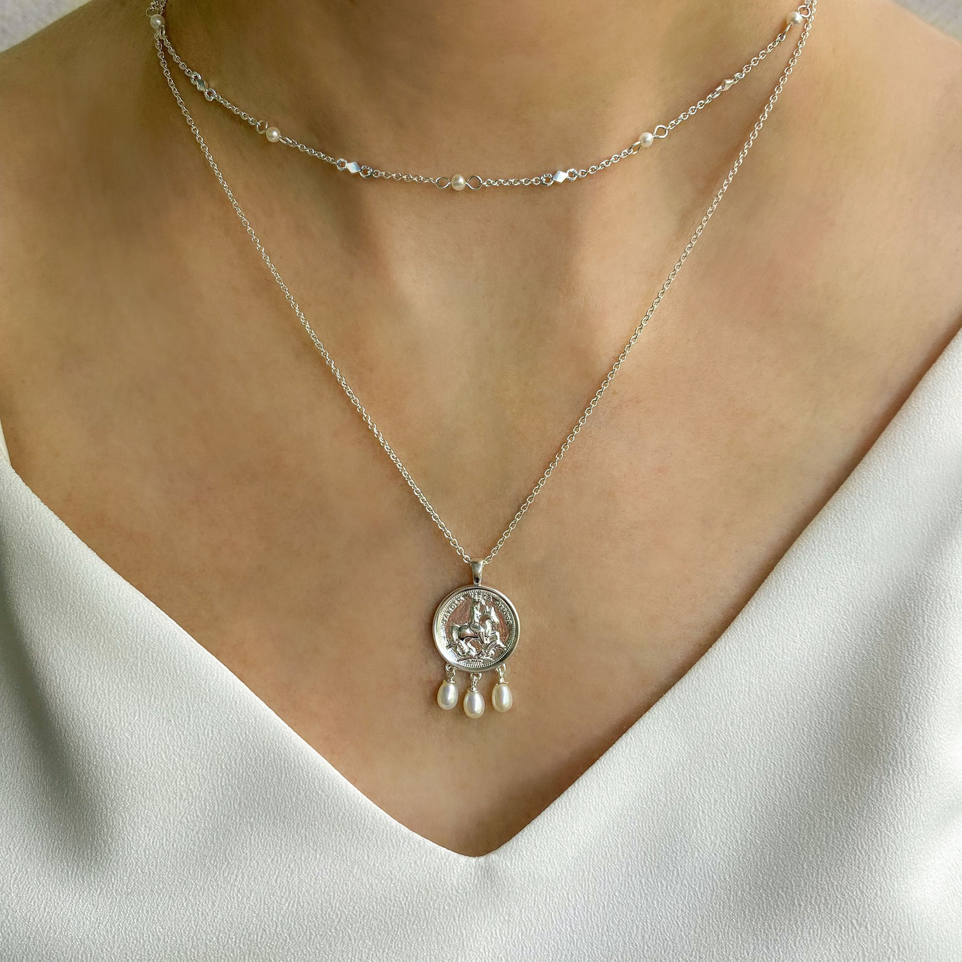 Model wearing silver beaded pearl choker necklace with engraved horse coin pendant necklace with hanging freshwater pearls