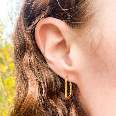 Model wearing gold contemporary rounded rectangle hoop earrings
